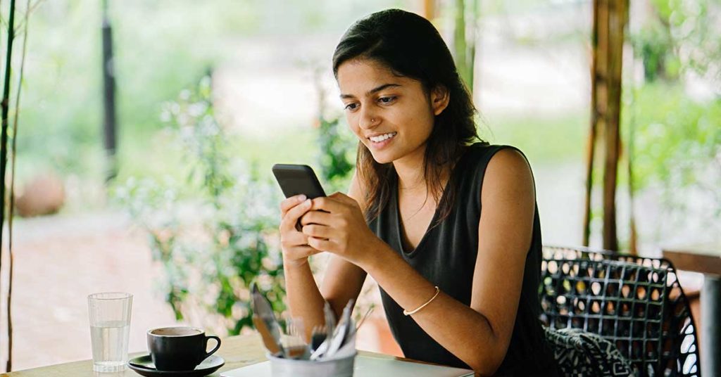 image of a woman with dark hair sitting on a covered patio looking at her phone