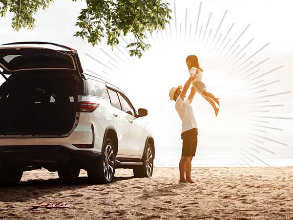 parent lifting child into the air next to an SUV on a beach