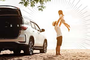 parent lifting child into the air next to an SUV on a beach