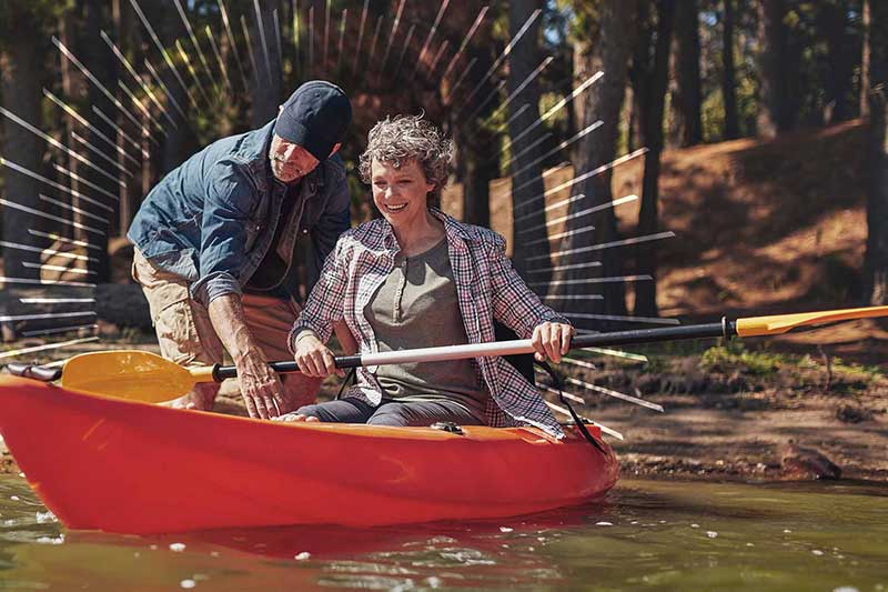 man standing in water helping a woman in a red kayak