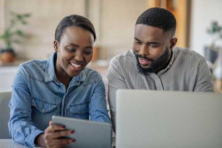 man and woman sitting next to each other smiling and looking at a tablet device